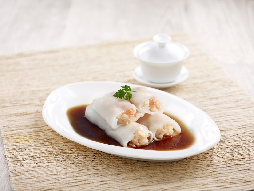 Plate of shrimp rice rolls in sauce with a teacup in the background.