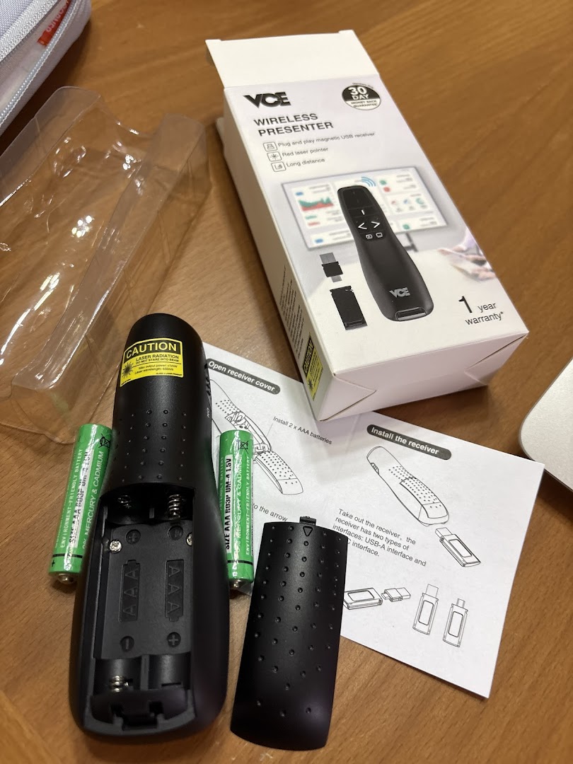 Wireless presenter, box, batteries, and instructions on a table.