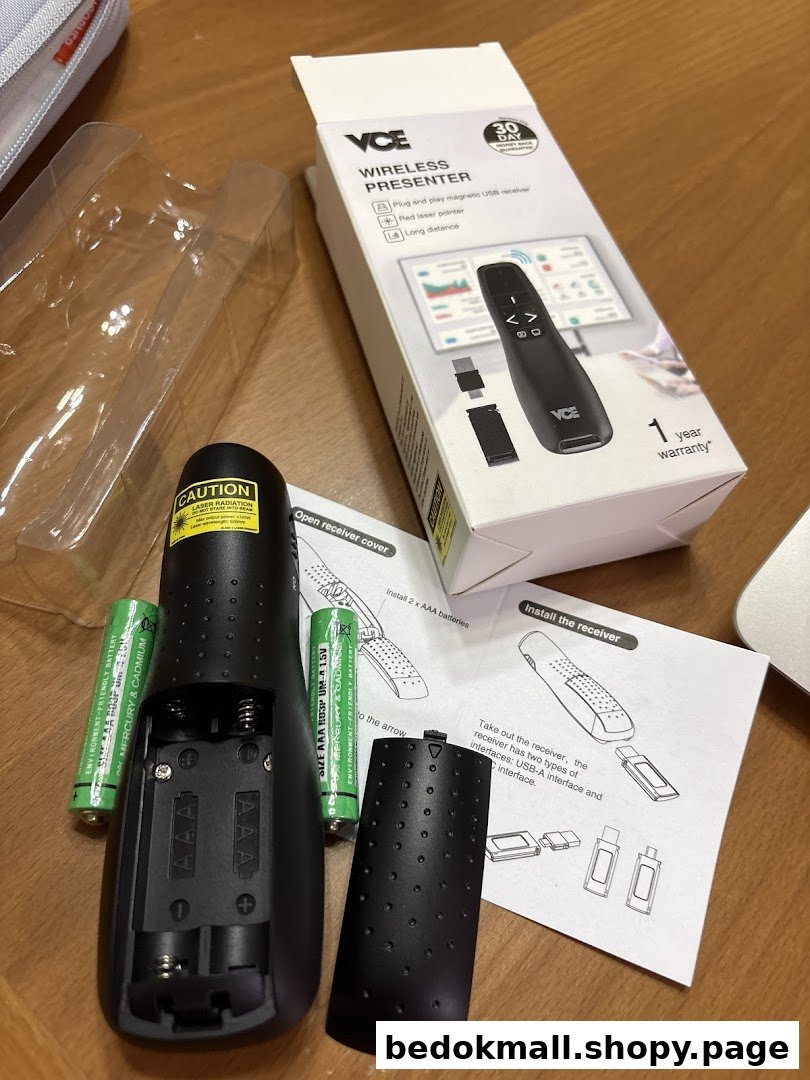 Wireless presenter, box, batteries, and instructions on a table.