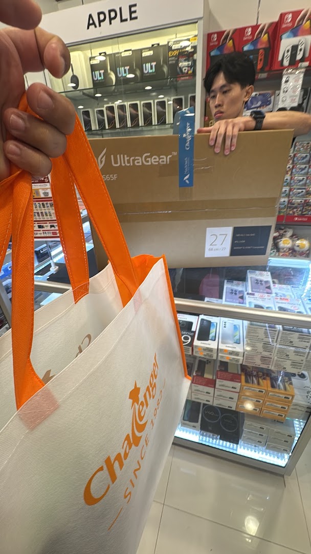 A person holding a Challenger bag inside an electronics store with products and staff.