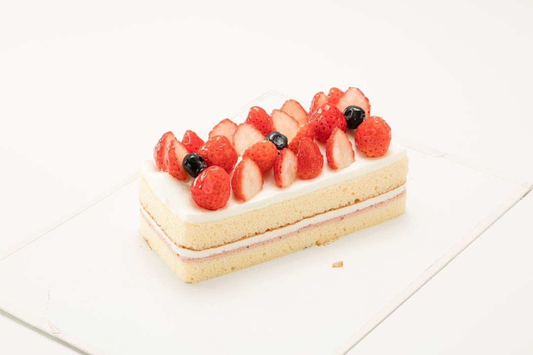 A rectangular cake topped with fresh strawberries and blueberries on a white background.
