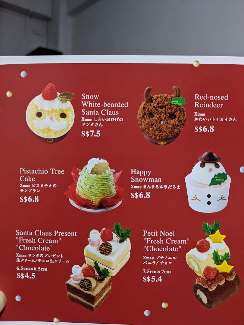 Close-up of a menu displaying various Christmas-themed cakes and their prices.