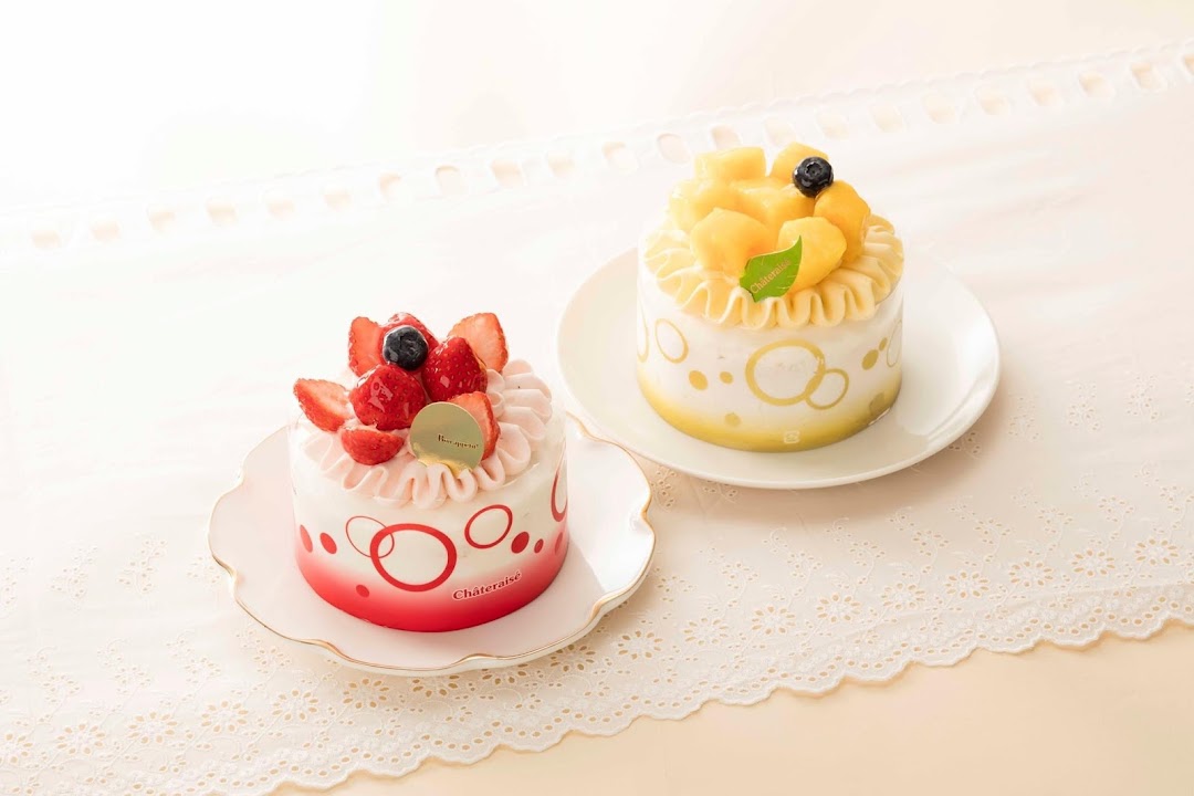Two decorated cakes, one strawberry and one mango, on white plates.