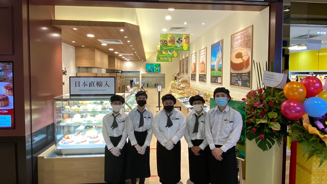 Staff members stand at the entrance of a bakery with display cases and cakes.