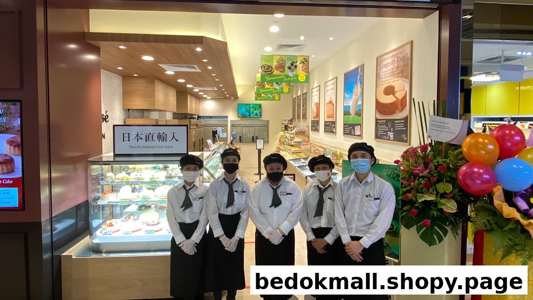 Staff members stand at the entrance of a bakery with display cases and cakes.
