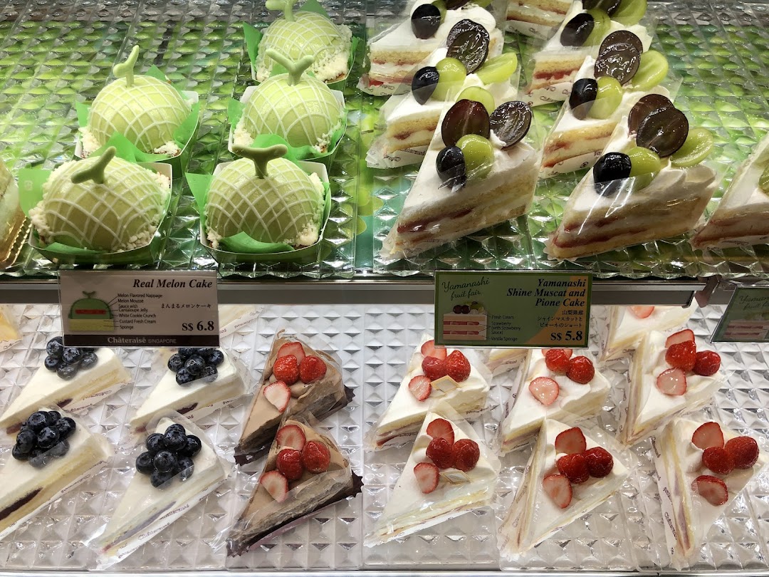 Display case filled with various cakes and pastries, including melon and fruit cakes.