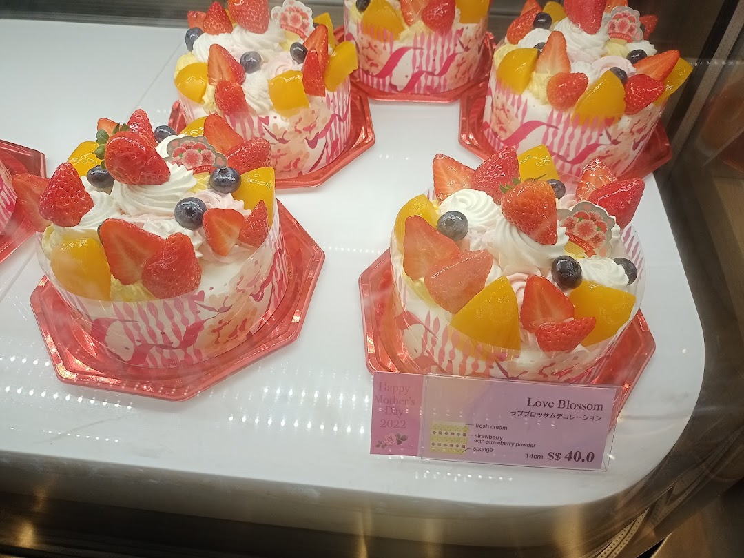 Multiple fruit-topped cakes displayed in a refrigerated case with a price tag.