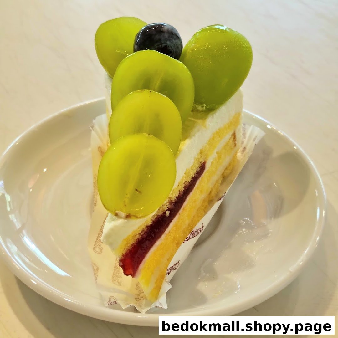 A slice of cake topped with green and one dark grape on a white plate.