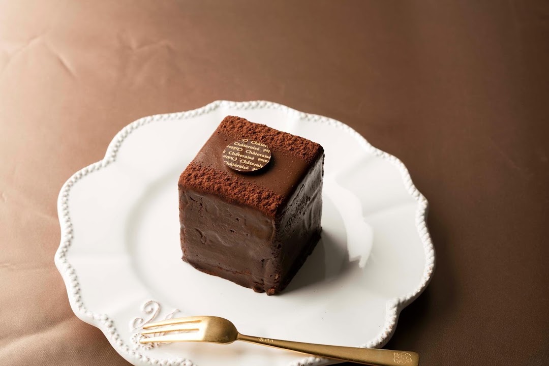 A chocolate cake on a white plate with a golden fork.