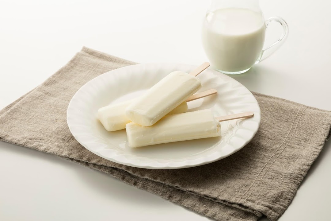 Three white popsicles on a plate with a pitcher of milk and napkin.