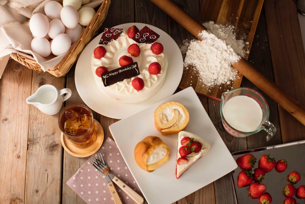 A flat lay of cakes, pastries, and baking ingredients on a wooden surface.