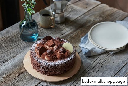 A chocolate cake on a rustic wooden table with coffee and plates.