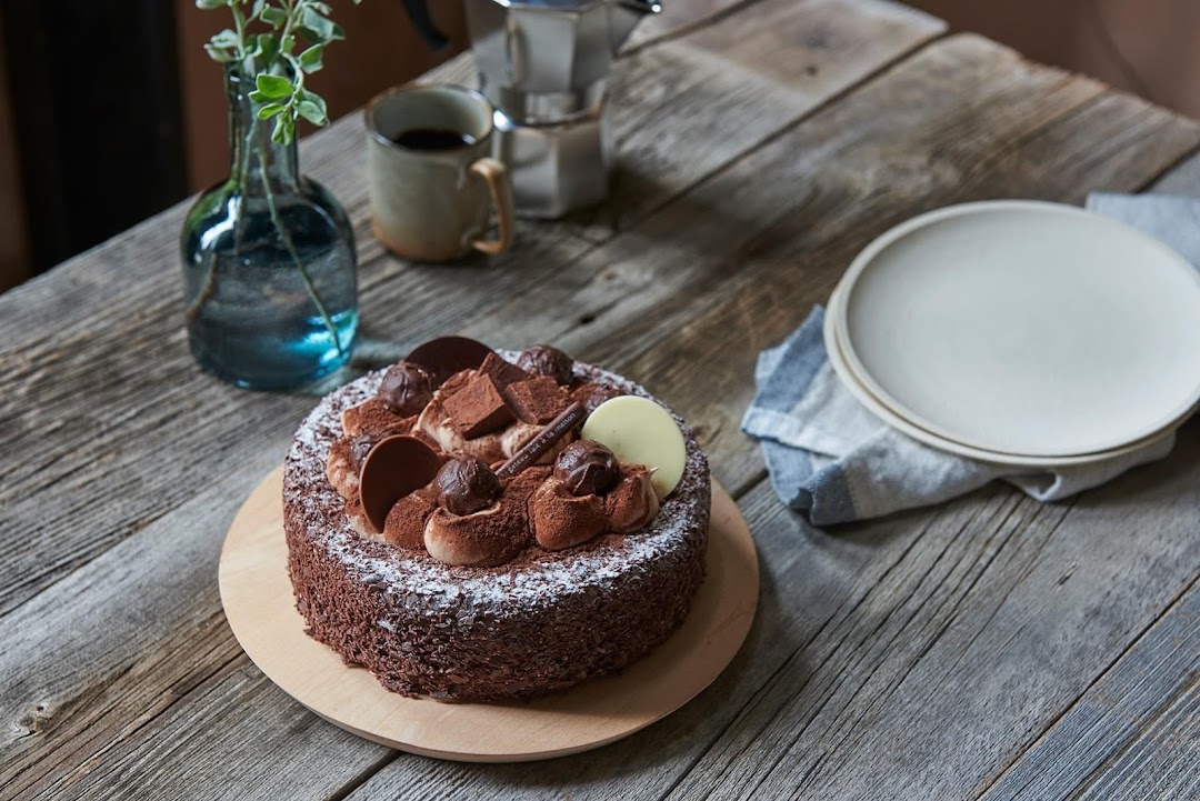 A chocolate cake on a rustic wooden table with coffee and plates.