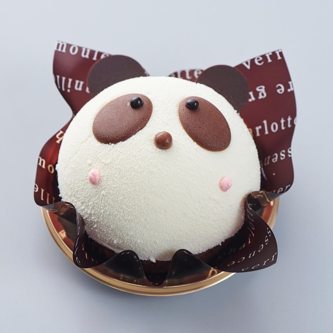 A white panda-shaped cake with chocolate features and pink cheeks on a gold plate.