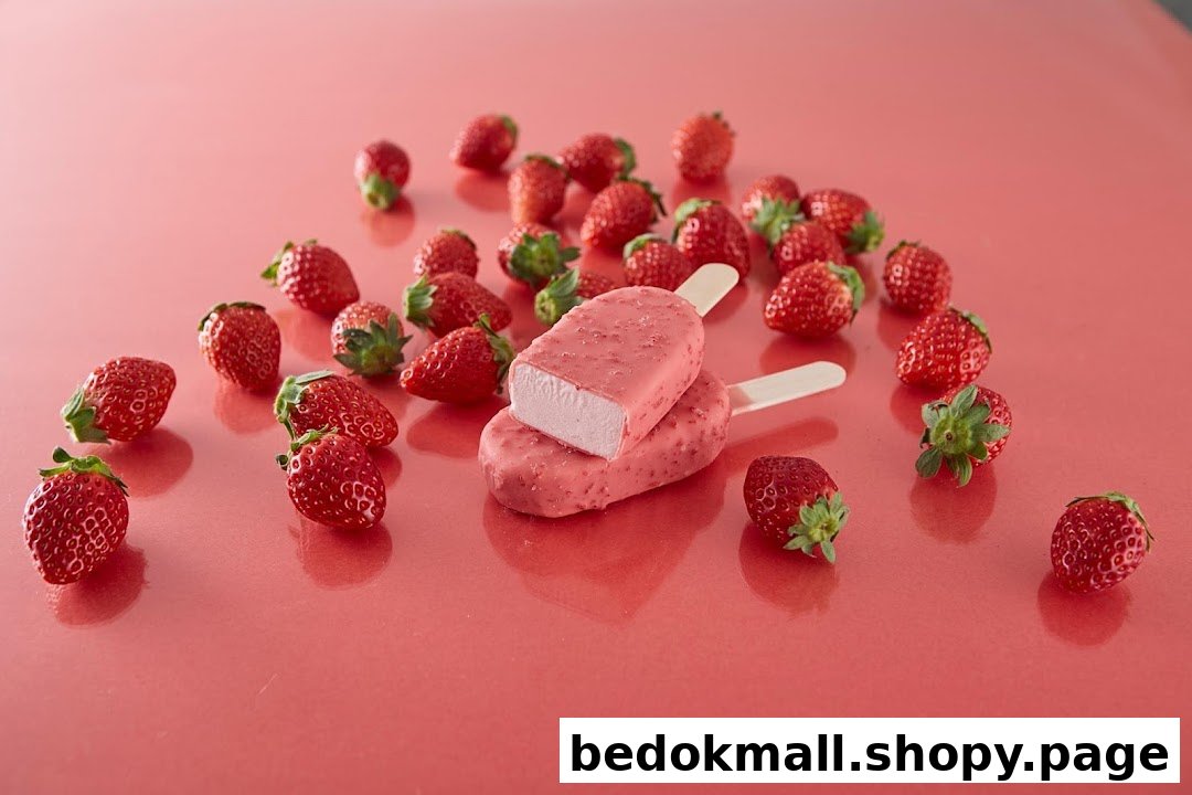 Pink ice cream bars and fresh strawberries scattered on a pink surface.
