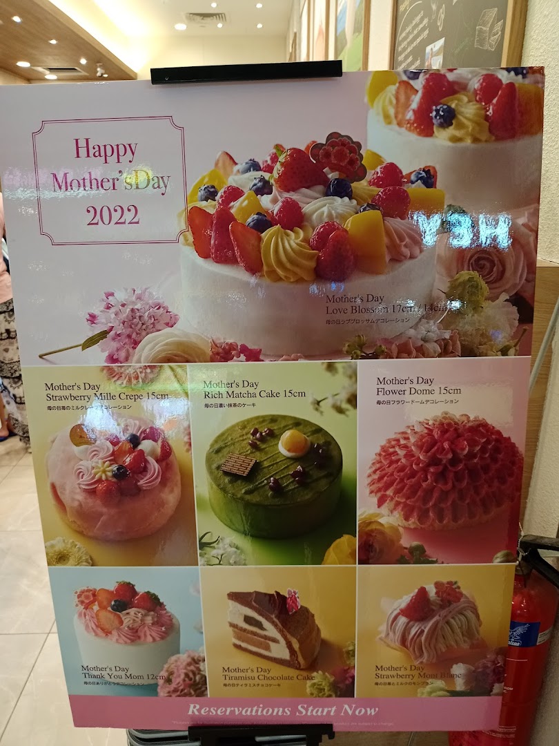 A display board showcasing various Mother's Day cakes with descriptions and prices.