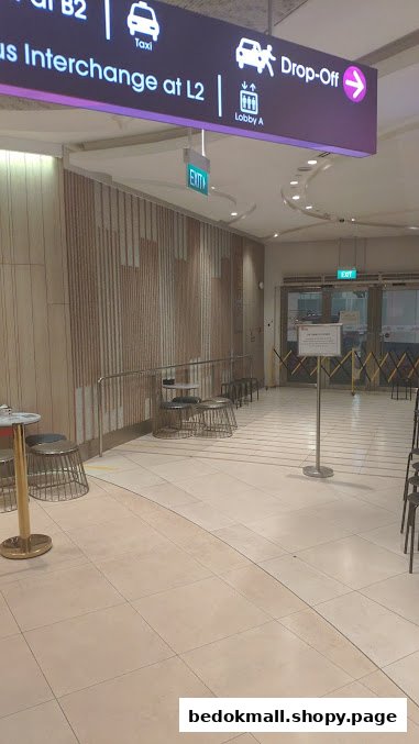 Indoor hallway with directional signs, seating, and an exit.