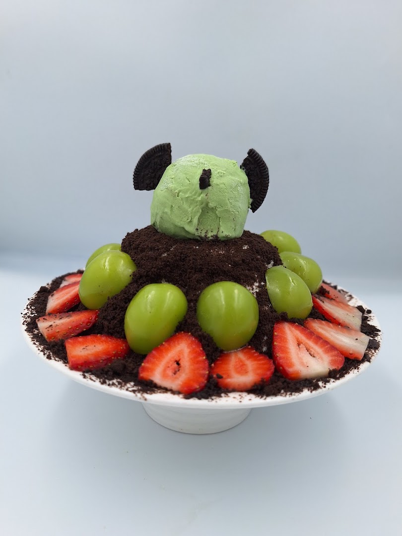 A dessert with green ice cream, cookie crumbs, grapes, and strawberries.