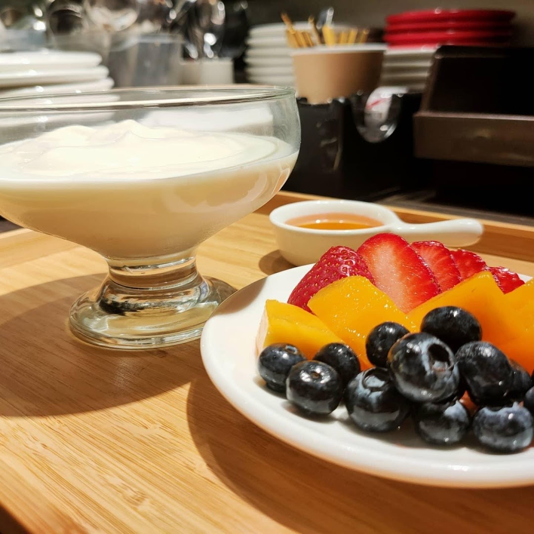 Yogurt with mixed berries, mango, and honey on a wooden tray.