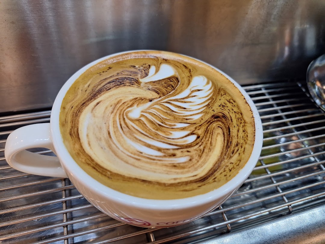 Close-up of a coffee cup with intricate latte art on a metal grate.