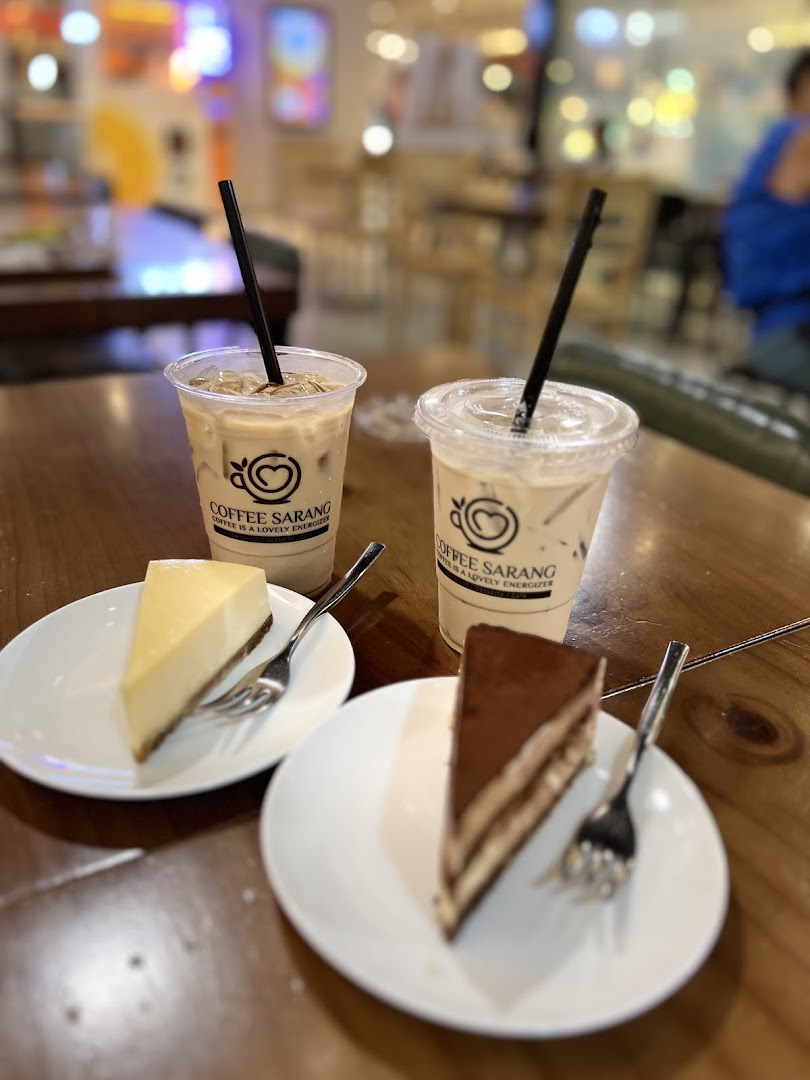 Two iced coffees and two cake slices on a wooden table inside a cafe.