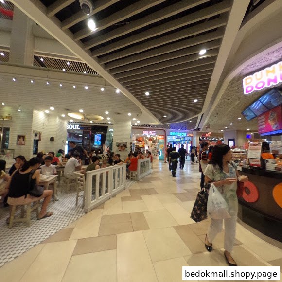 Interior view of a busy mall food court with people dining and walking.