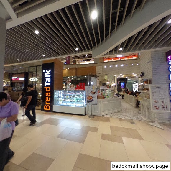 Interior view of a shopping mall with various shops and people.