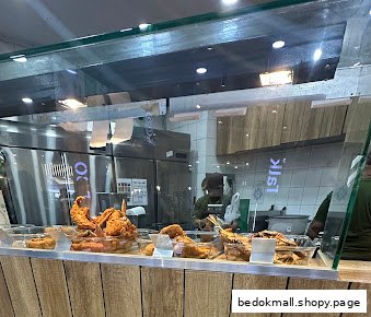 Food counter displaying fried chicken with kitchen area in the background.