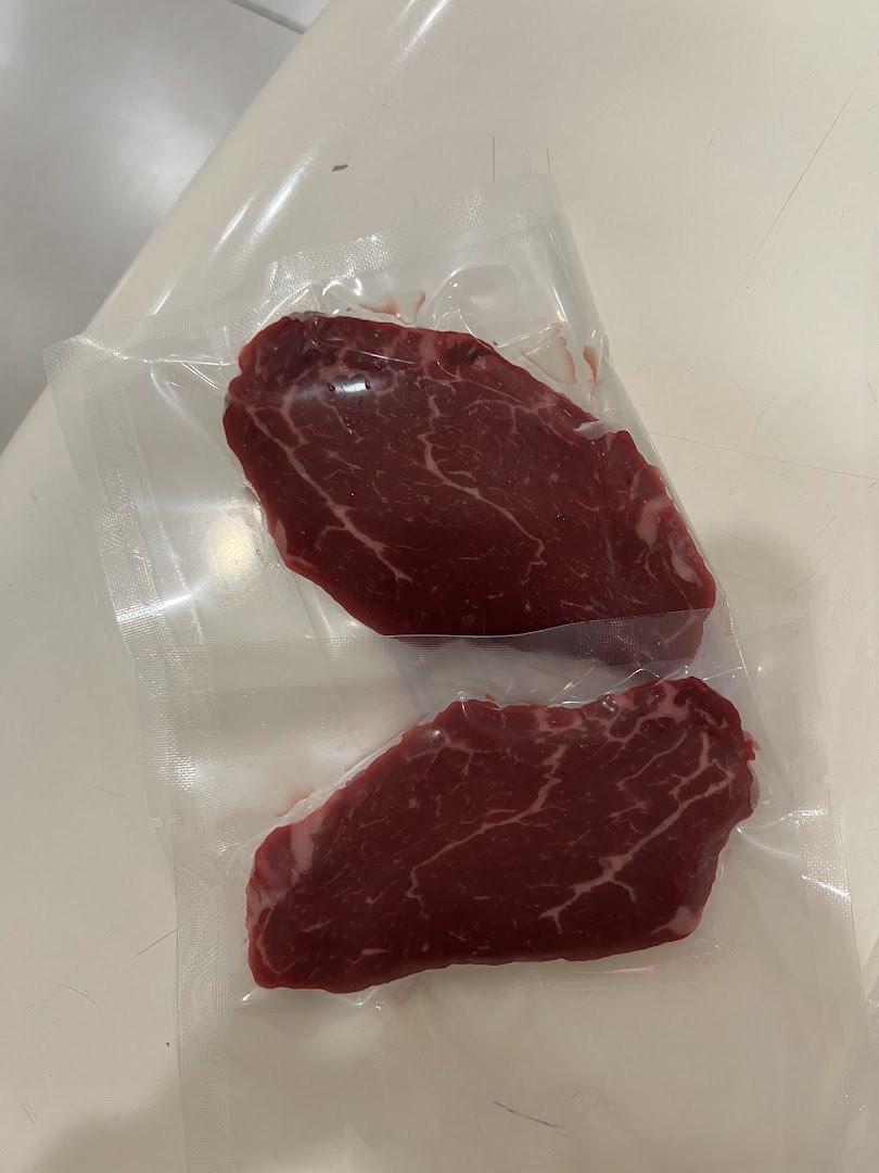 Two vacuum-sealed steaks in clear plastic packaging on a white surface.