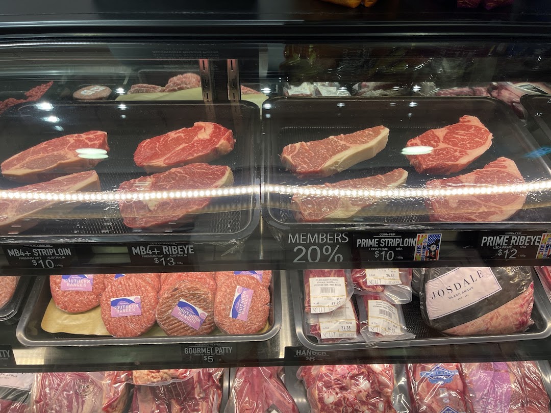 A refrigerated display case filled with various cuts of fresh meat and price labels.