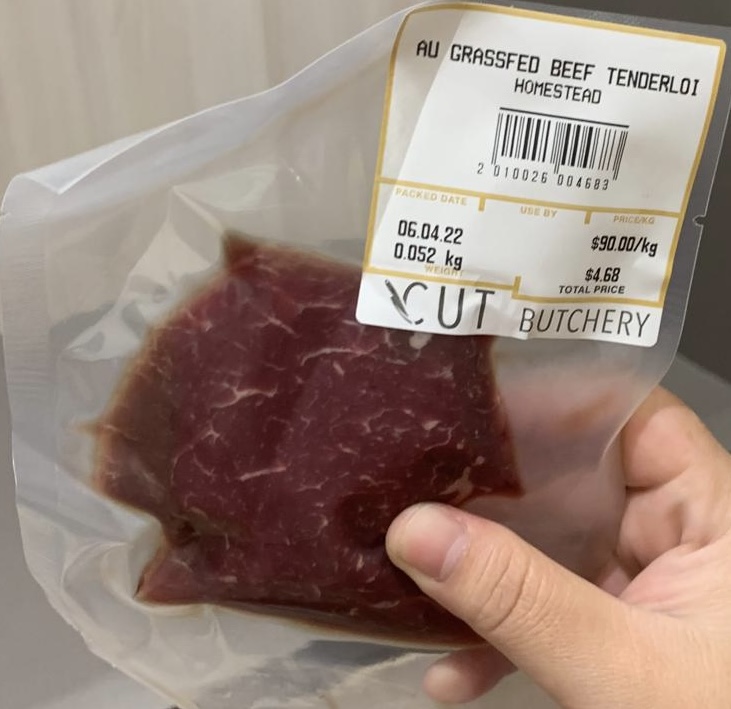 A hand holds a vacuum-sealed beef tenderloin package with a price label.