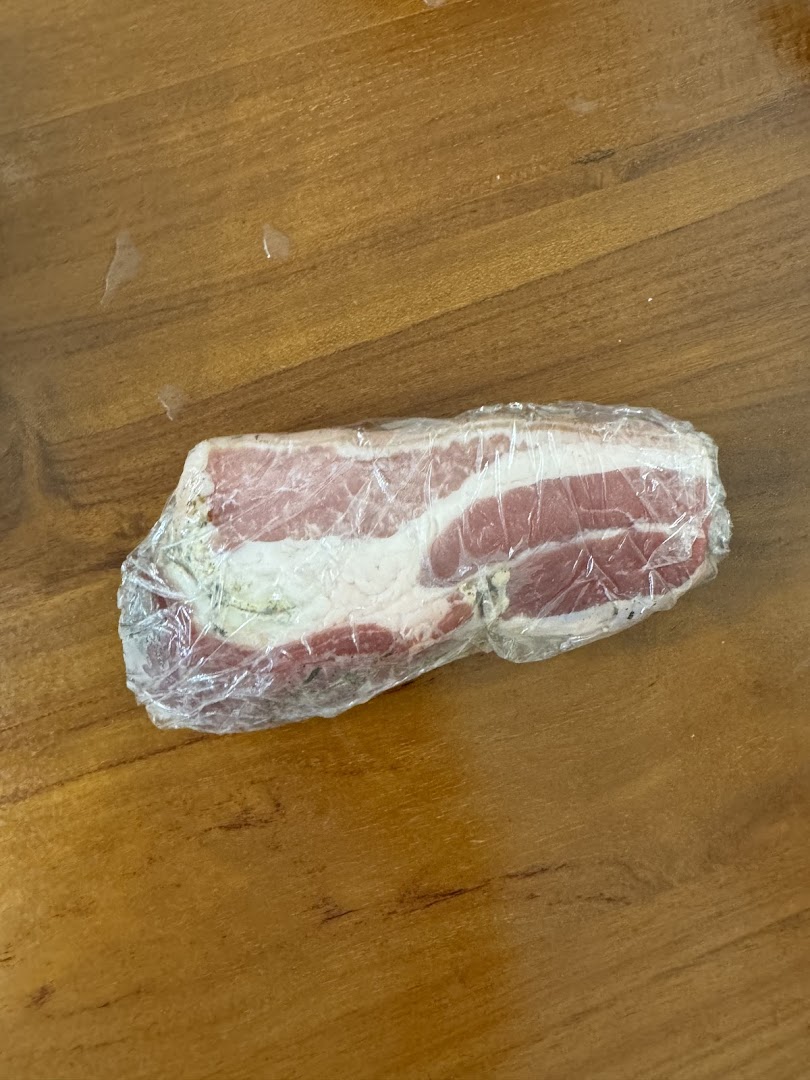 A piece of raw meat wrapped in plastic on a wooden surface.