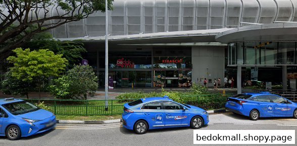 Exterior view of a shopping center with multiple shop entrances and taxis.