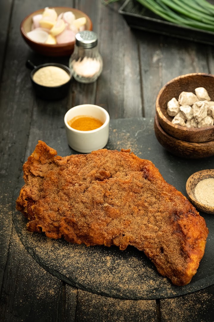 A large seasoned fried chicken cutlet with various ingredients and condiments.