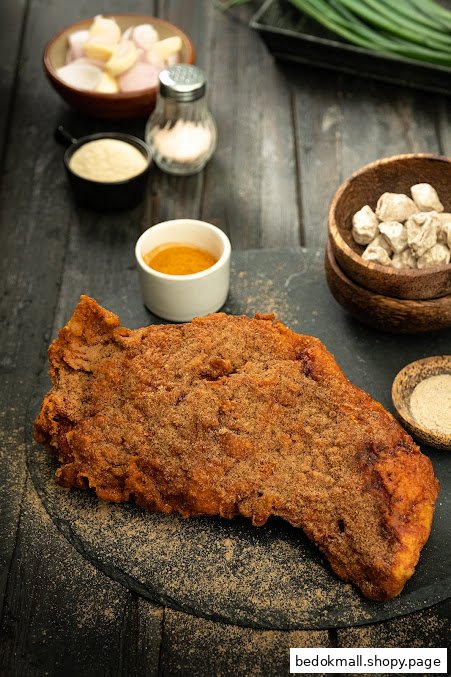 A large, seasoned fried chicken cutlet on a dark surface with condiments.
