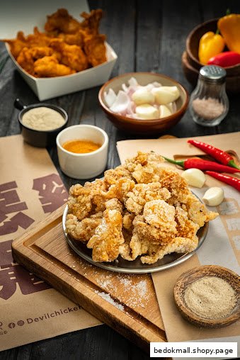 Fried chicken pieces with spices and ingredients on a dark wooden surface.