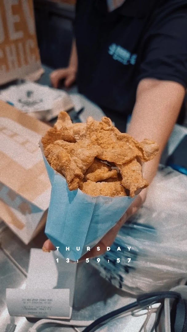 A person holds a blue bag filled with fried chicken pieces.