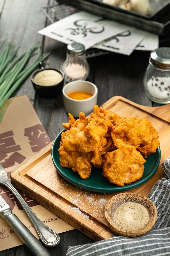 A plate of golden fried chicken pieces with sauces and spices on a wooden board.
