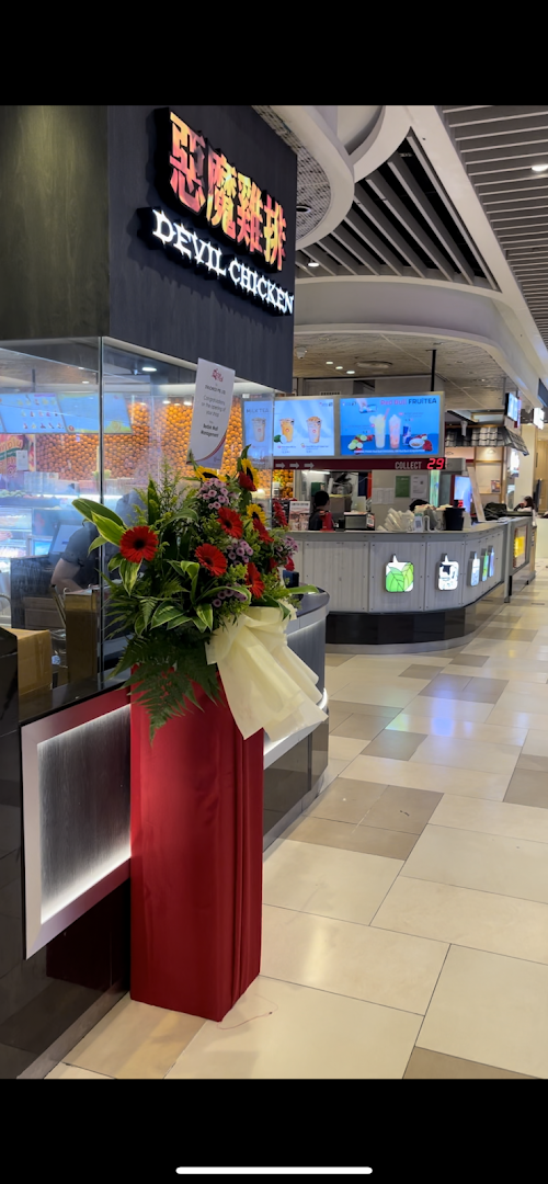 Interior view of a mall with a "Devil Chicken" shop and a flower arrangement.