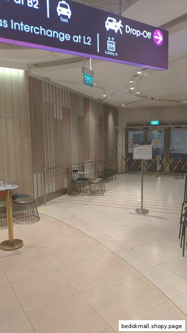Indoor hallway with navigation signs, seating, and glass doors.