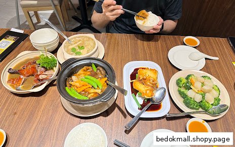 A table filled with various Chinese food dishes and a person eating.