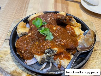 Fried fish with sauce and onions served on a hot plate.