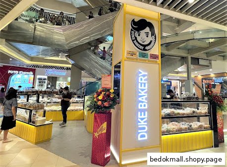 Bakery stall with display cases and customers inside a shopping mall.