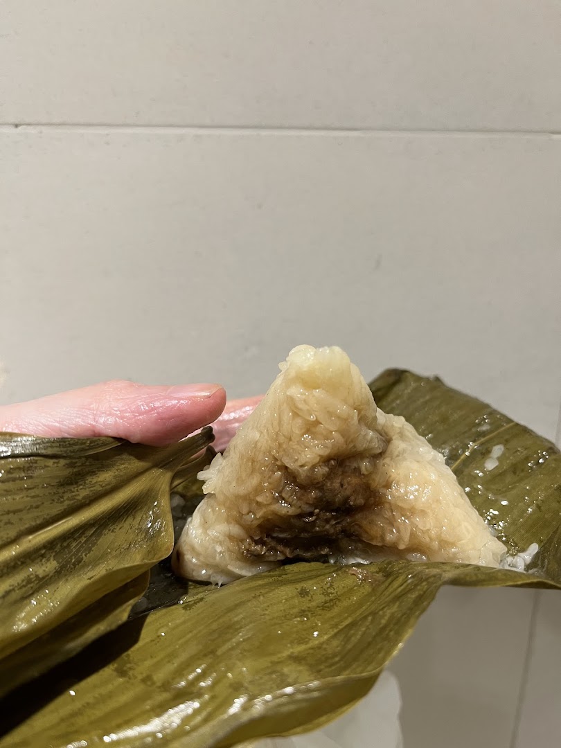 Hand holding a partially unwrapped rice dumpling in leaf packaging.