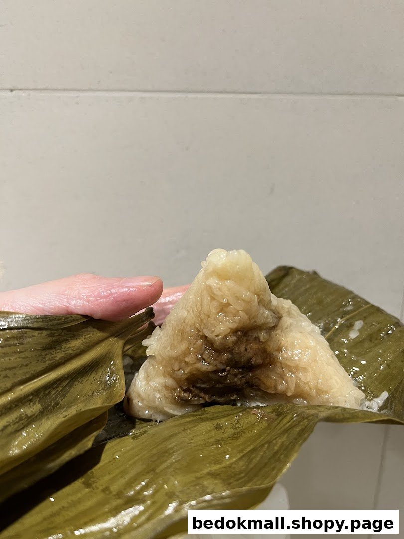 Hand holding a partially unwrapped rice dumpling in leaf packaging.