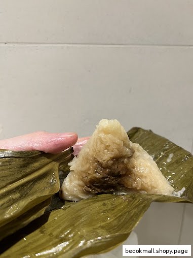 A hand holds an unwrapped rice dumpling (zongzi) in its leaves.