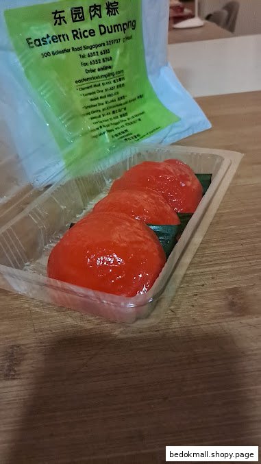 Red dumplings in a plastic container with a green bag showing shop information.