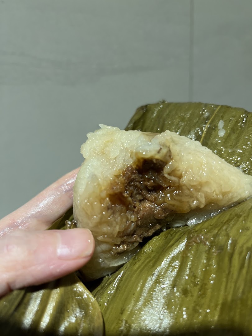 A hand holds a partially unwrapped rice dumpling (zongzi) with a savory filling.