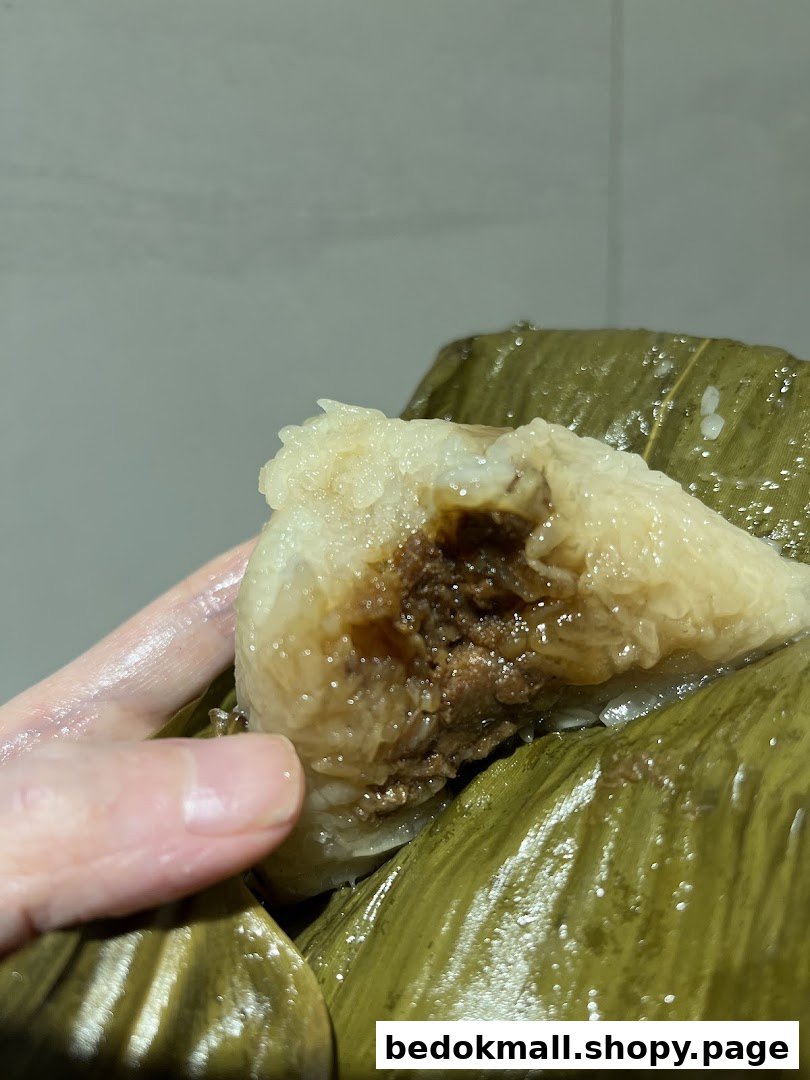 A hand holds a partially unwrapped rice dumpling (zongzi) with a savory filling.