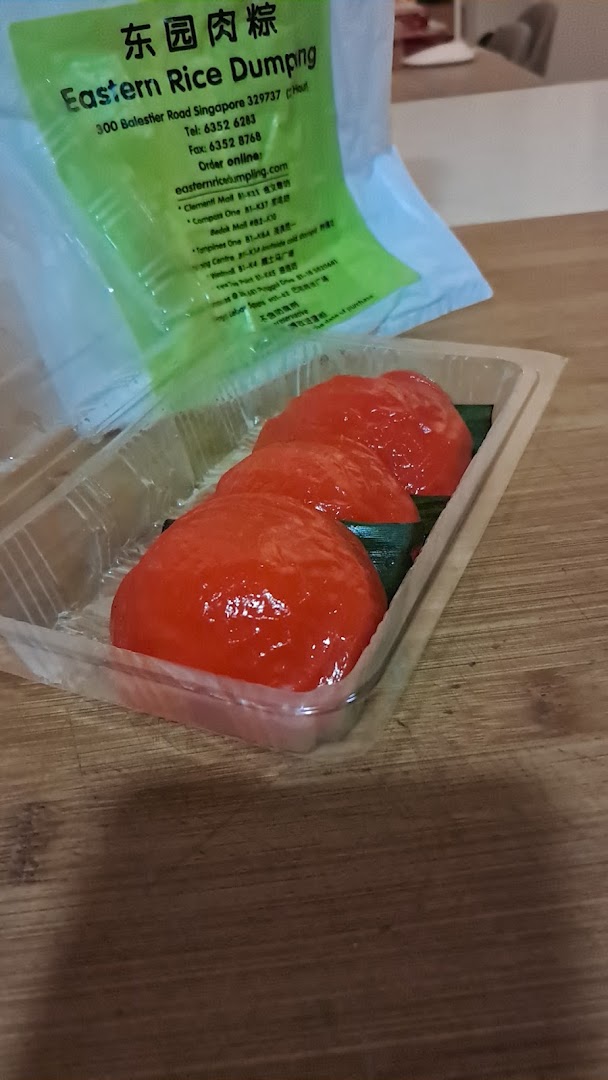 Three red kueh in a plastic container with shop packaging.
